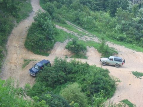 1994 Ford Bronco - Two off-road vehicles navigate a winding dirt path through a wooded area.