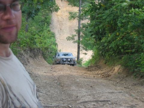 1994 Ford Bronco - A 1994 Ford Bronco navigates a steep, muddy incline on a wooded trail.