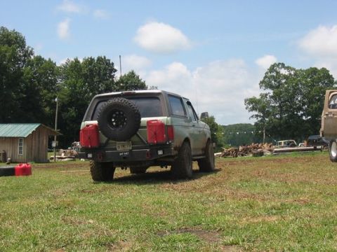 1994 Ford Bronco - Green Ford Bronco with spare tire and jerry cans parked in a field, another vehicle visible to the right.