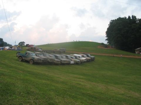 1994 Ford Bronco - A row of trucks are parked on a grassy slope under a cloudy sky.