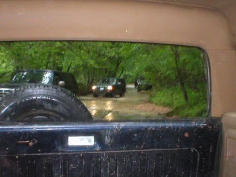 1994 Ford Bronco - Multiple SUVs navigate a wet, wooded path, suggesting an off-road excursion.