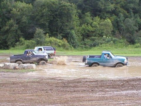 1994 Ford Bronco - Several off-road vehicles navigate a muddy track during an event.