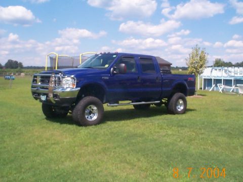 1978 Ford Bronco - Blue 2003 Ford F-250 Super Duty pickup truck with chrome grille guard parked on grass.