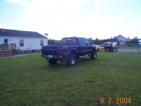 1978 Ford Bronco - Lifted blue Ford F-250 Super Duty pickup truck is parked in a grassy yard with other vehicles visible.