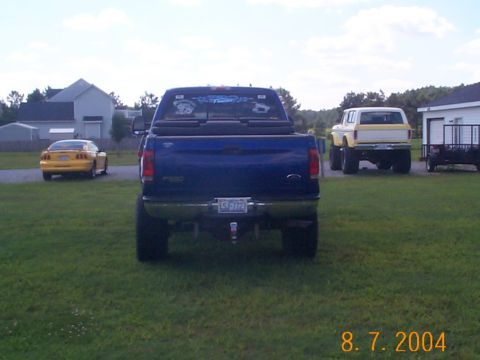 1978 Ford Bronco - A blue Ford F-250 pickup truck is parked in a grassy yard with other vehicles visible in the background.