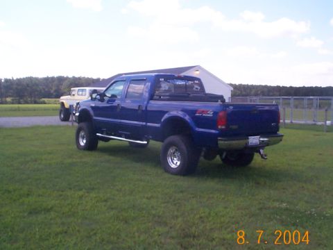 1978 Ford Bronco - A blue Ford F-250 Super Duty pickup truck is parked on a grassy field next to a white SUV.