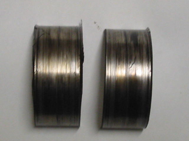 Two worn metal engine bearing shells on a gray surface