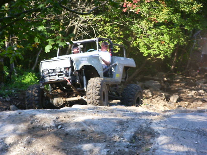 White caged open-top 4x4 with winch and mud tires crawling over rocks on a trail