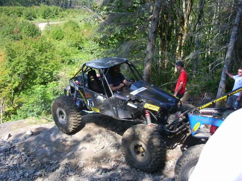 1990 Ford Bronco - A black tube-chassis rock buggy numbered 79 crawls across a rocky quarry ledge with two crew aboard in helmets and harnesses. Red coilover…