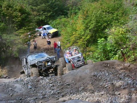1990 Ford Bronco - Multiple off-road vehicles navigate a challenging rocky terrain on a sunny day.