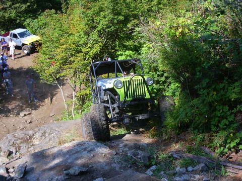 1990 Ford Bronco - An off-road buggy tackles a challenging rocky incline, with a pickup truck and onlookers observing the action.