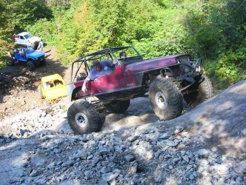 1990 Ford Bronco - A maroon Jeep Wrangler stripped to a bare tub with an exposed roll cage, chopped fenders and no hood or grille shell crawls up a slab of be…