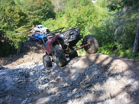 1990 Ford Bronco - Several off-road vehicles navigate a steep, rocky incline on a wooded trail.