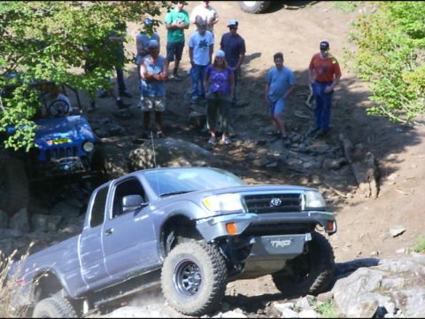 1990 Ford Bronco - A silver Toyota Tacoma extended-cab pickup with a TRD skid plate climbs a rocky ledge on a trail, front end flexed with mud-terrain tires o…