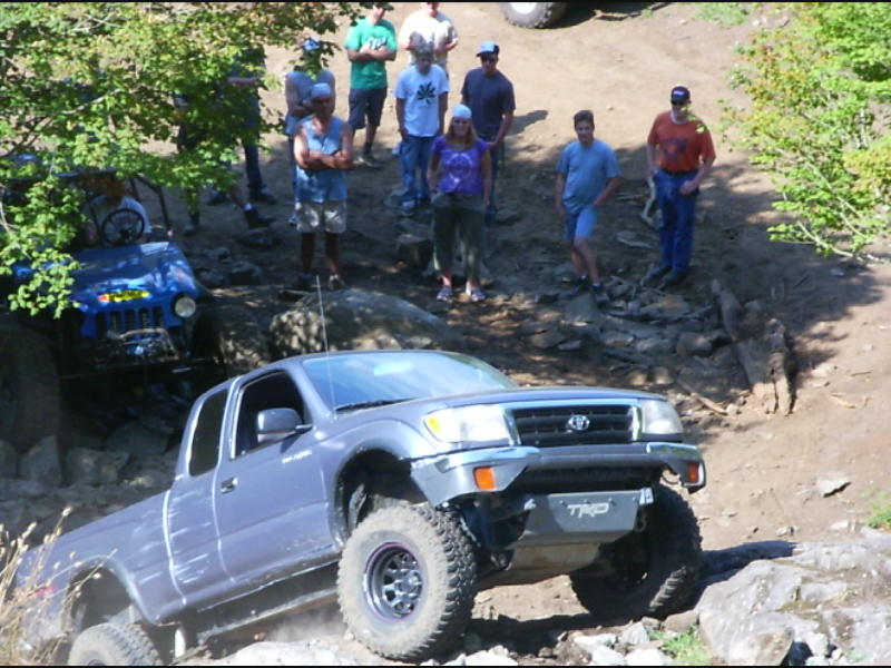 Silver Toyota Tacoma with TRD skid plate climbing a rocky ledge as spectators watch