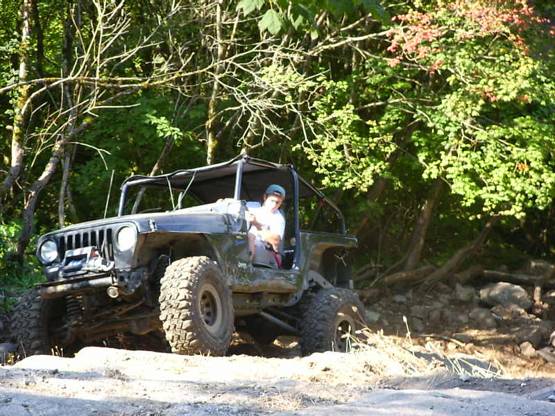 Modified Jeep Wrangler on a dirt trail with trees in the background