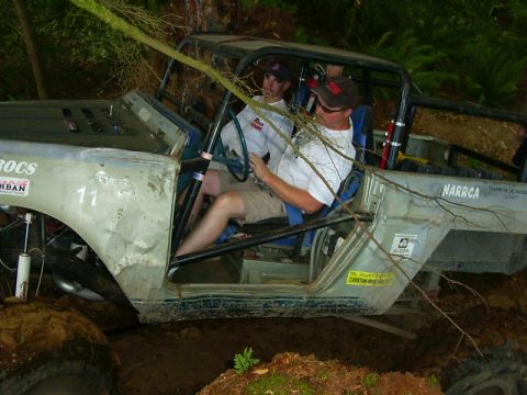 1990 Ford Bronco - Overhead view into the open cockpit of a mud-splattered white doorless Jeep-style rock crawler with a full black roll cage, blue vinyl buck…