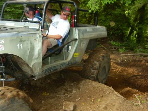 1990 Ford Bronco - Close side view of a battered white doorless 4x4 numbered 11 on the front fender, crawling through a dirt trench with the driver in a blue…
