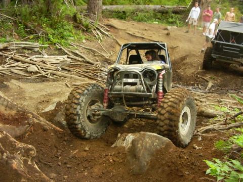 1990 Ford Bronco - Head-on view of a black tube-frame buggy dropping down a dirt trail, showing its exposed front axle, tube bumper with mounted winch and red…