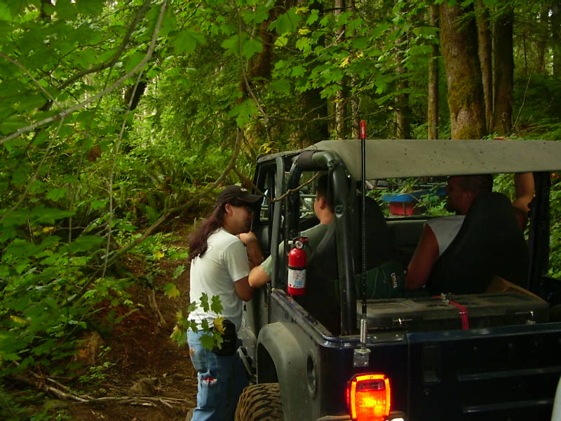 Dark caged open-top 4x4 on a wooded trail with fire extinguisher and whip antenna