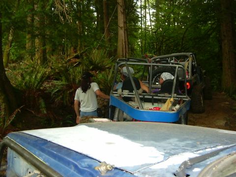 1990 Ford Bronco - Off-road vehicles are parked on a forest trail with people inside.