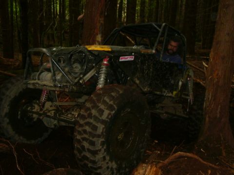 1990 Ford Bronco - A heavily modified off-road vehicle navigates a wooded terrain with large tires and a visible roll cage.
