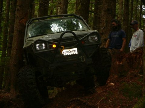 1990 Ford Bronco - Modified off-road vehicle navigating a wooded trail with two people observing.