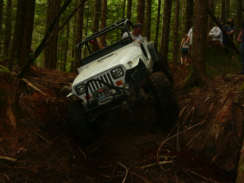 White Jeep Wrangler TJ off-roading on a muddy, wooded trail