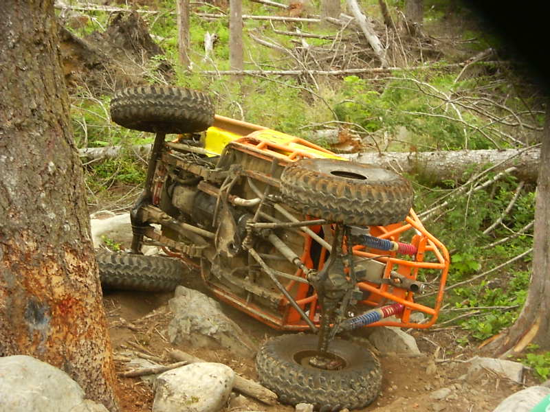 Orange off-road buggy overturned on a rocky, wooded trail