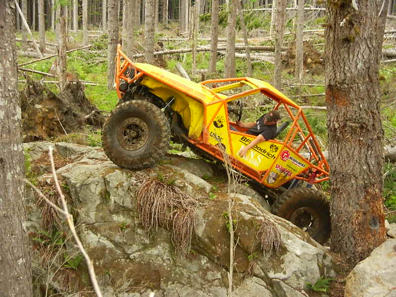 Yellow off-road buggy with roll cage climbing over large rocks in a forest