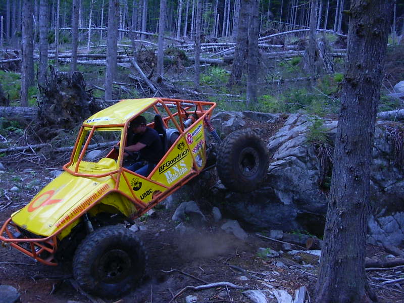 Yellow off-road buggy with orange roll cage climbing rocks, BFGoodrich tires visible