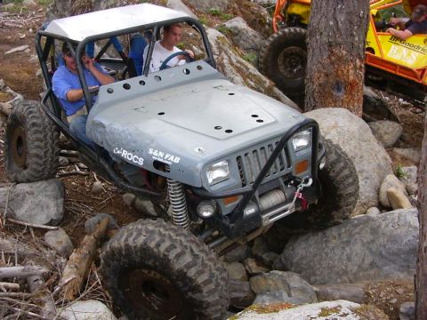 1990 Ford Bronco - This heavily modified off-road vehicle, possibly a Jeep, navigates a challenging rocky terrain with another vehicle visible in the backgrou…