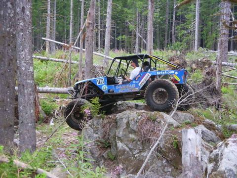 1990 Ford Bronco - Off-road buggy navigates a rocky trail in a wooded area.