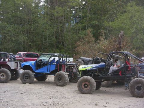 1990 Ford Bronco - Custom off-road buggies are lined up on a dirt surface, with a wooded area behind them.