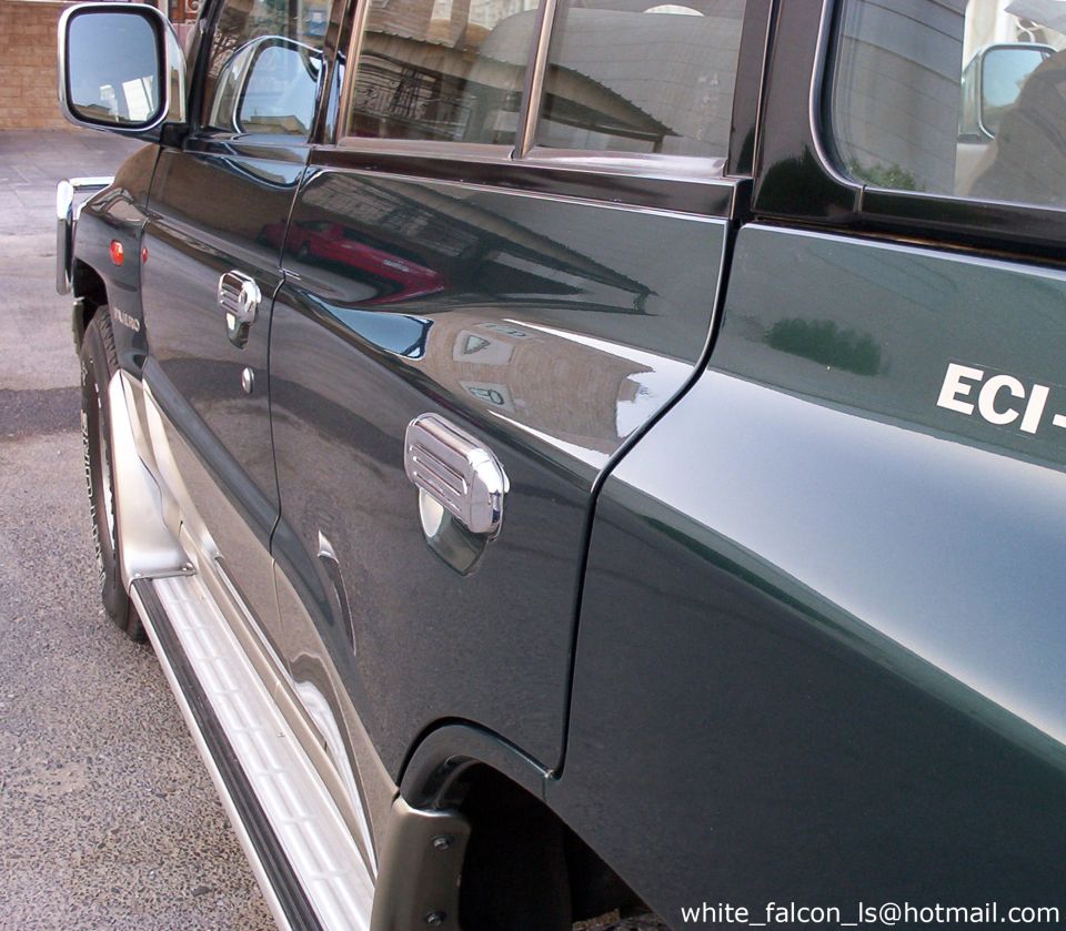 Side view of a dark green Mitsubishi Pajero SUV with chrome handles and side step