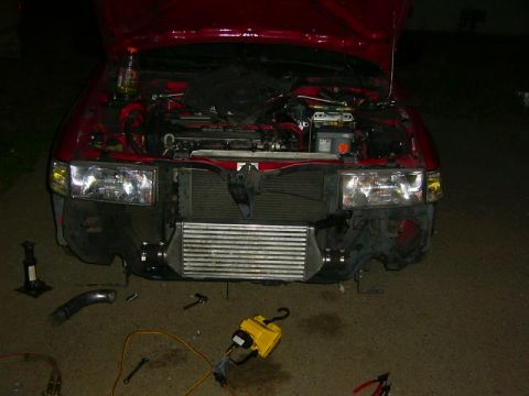 1990 Ford Bronco - Front end of a red vehicle with the hood open, showing the engine bay and an installed intercooler, with various tools on the ground.