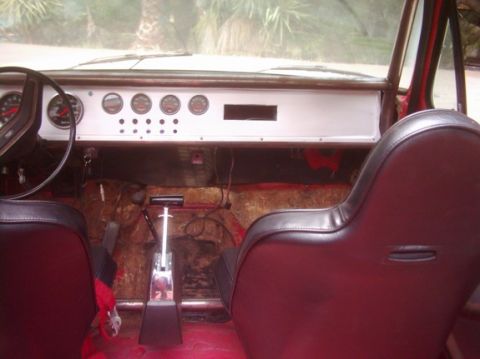 1978 Ford Bronco - Stripped-out interior of an open-top 4x4 shot from the rear seat, showing a white custom dash panel with a row of four round aftermarket ga…