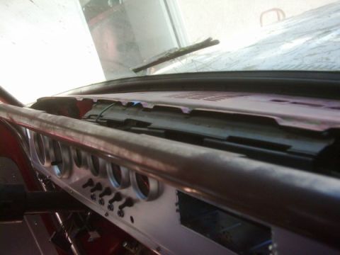 1978 Ford Bronco - Low-angle interior shot across a truck dashboard toward the windshield, showing a row of round gauge bezels and toggle switches on a bare m…