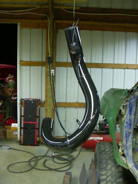 1990 Ford Bronco - A large, shiny black exhaust pipe is suspended in a workshop, with parts of a vehicle visible nearby.