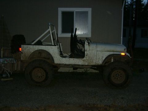 1990 Ford Bronco - This muddy white Jeep CJ is seen from the side, a roll cage and off-road tires.