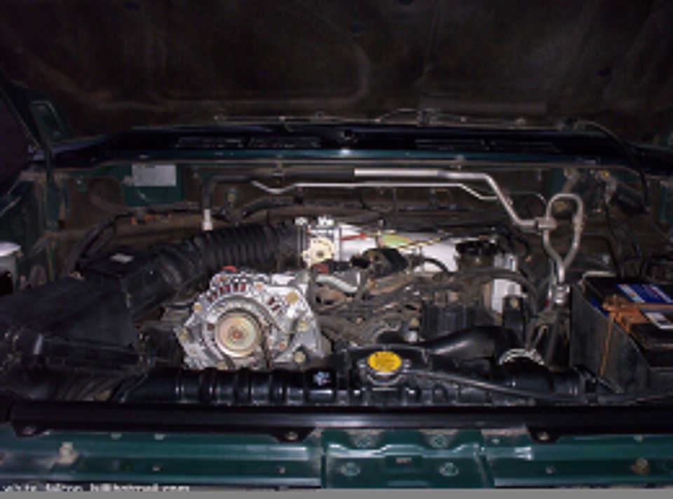Engine bay of a green SUV showing alternator, intake tube, radiator and battery