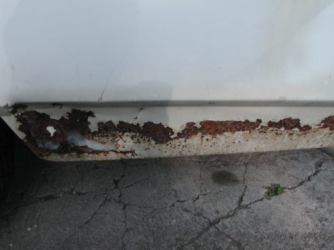 1988 Ford Crown Victoria - The lower body panel of a white vehicle shows significant corrosion and damage.