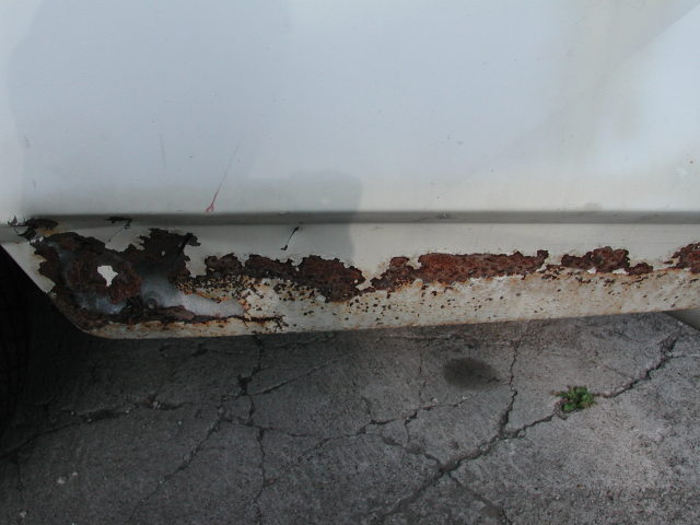 White car rocker panel with extensive rust damage and peeling paint