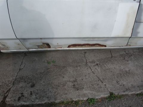 1988 Ford Crown Victoria - Rust is visible on the lower panel of a white car door, indicating significant body damage.