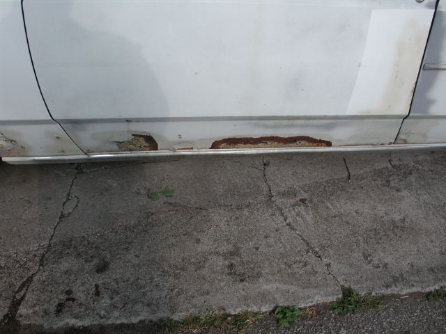 White car door with rust damage on the lower panel and trim