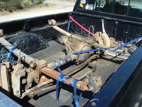 1989 Ford Bronco - Vehicle front axle assembly, likely for a 4x4, is strapped down in the bed of a pickup truck.
