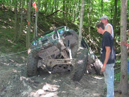 1992 Ford Bronco - An off-road vehicle is stuck in thick mud on a wooded trail as two onlookers observe the situation.