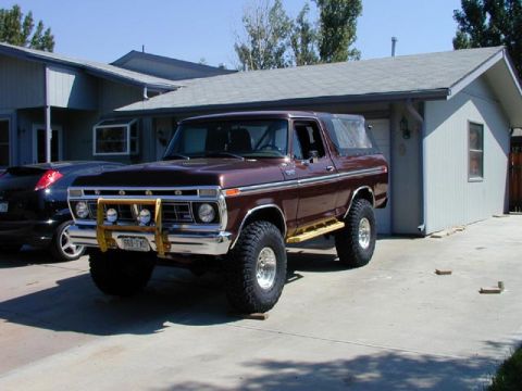 1979 Ford Bronco - This lifted Ford Bronco features a prominent yellow bull bar and side steps, parked in front of a residential garage.