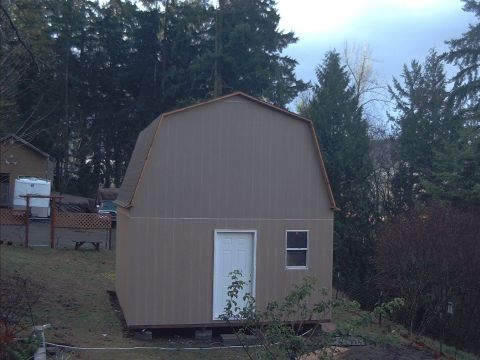 1977 Ford F-150 - A barn-style shed is situated on a sloped yard, surrounded by trees under a cloudy sky.
