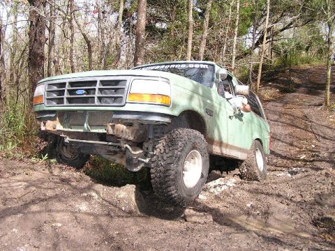 1994 Ford Bronco - A green Ford Bronco navigates a muddy incline in a wooded area.